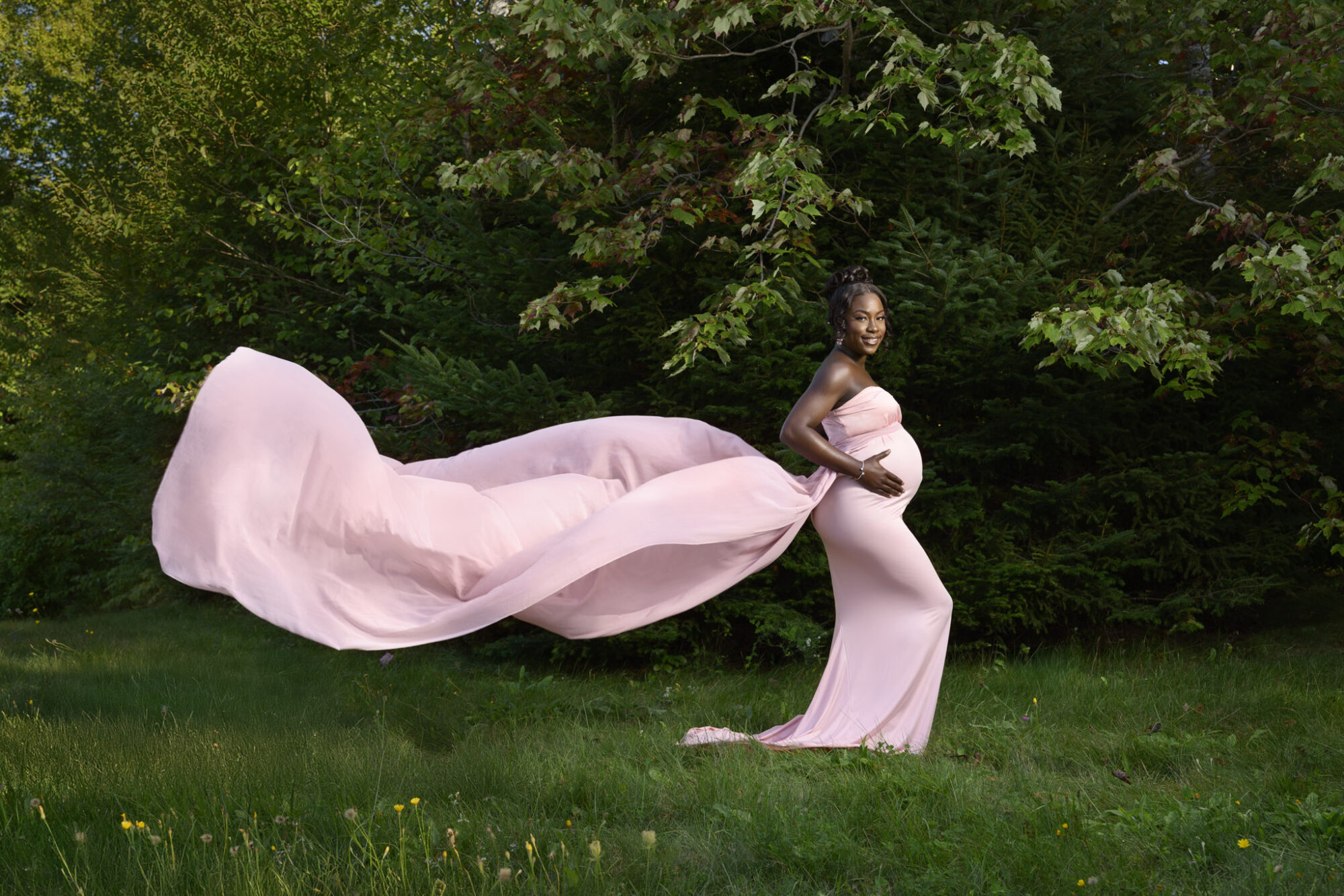 Mother to be wearing long pink dress with a flowing chiffon train blowing in the wind