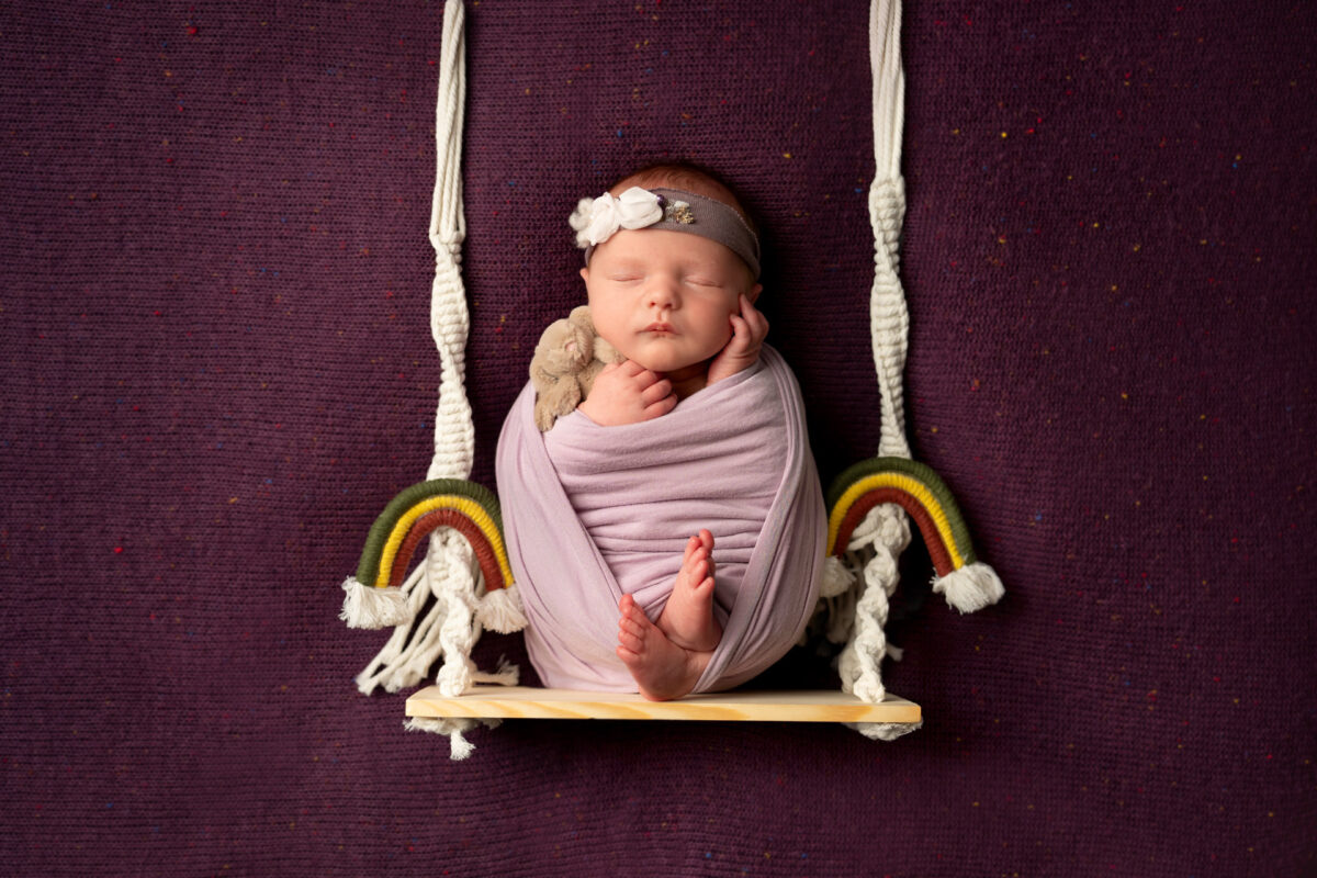 Newborn baby on a swing with rainbows