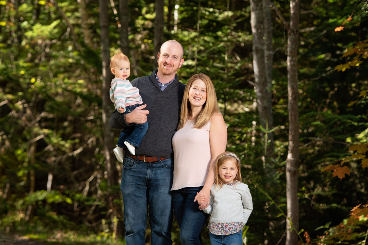 Family wearing gray and pink on a wooded trail posing for a photo